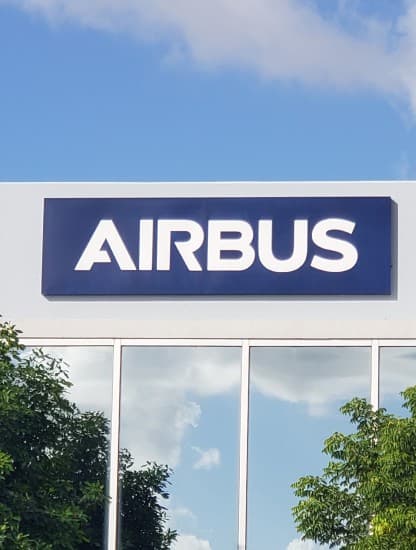 The Airbus wordmark on a sign above a building's glazed entrance, trees reflected in the glass below.