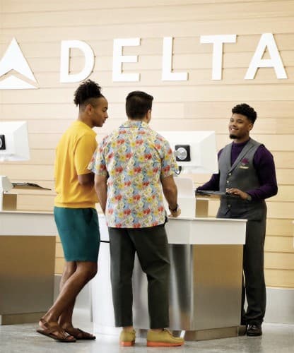 Passengers being helped at a Delta check-in desk in front of a wordmark wall.