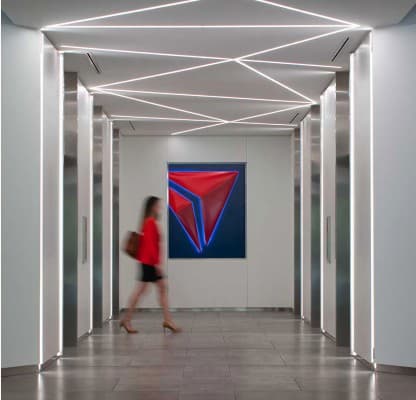 A woman walking through an illuminated elevator lobby past a red and blue Delta-branded artwork.