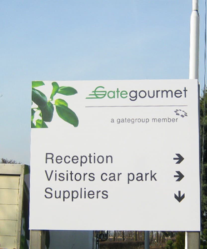 A Gate Gourmet wayfinding sign for reception, visitor parking and suppliers, mounted on a post.