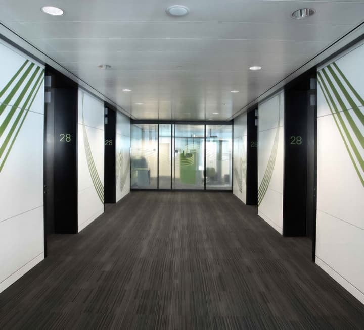 A dark office corridor, its walls striped with green leaf graphics either side.