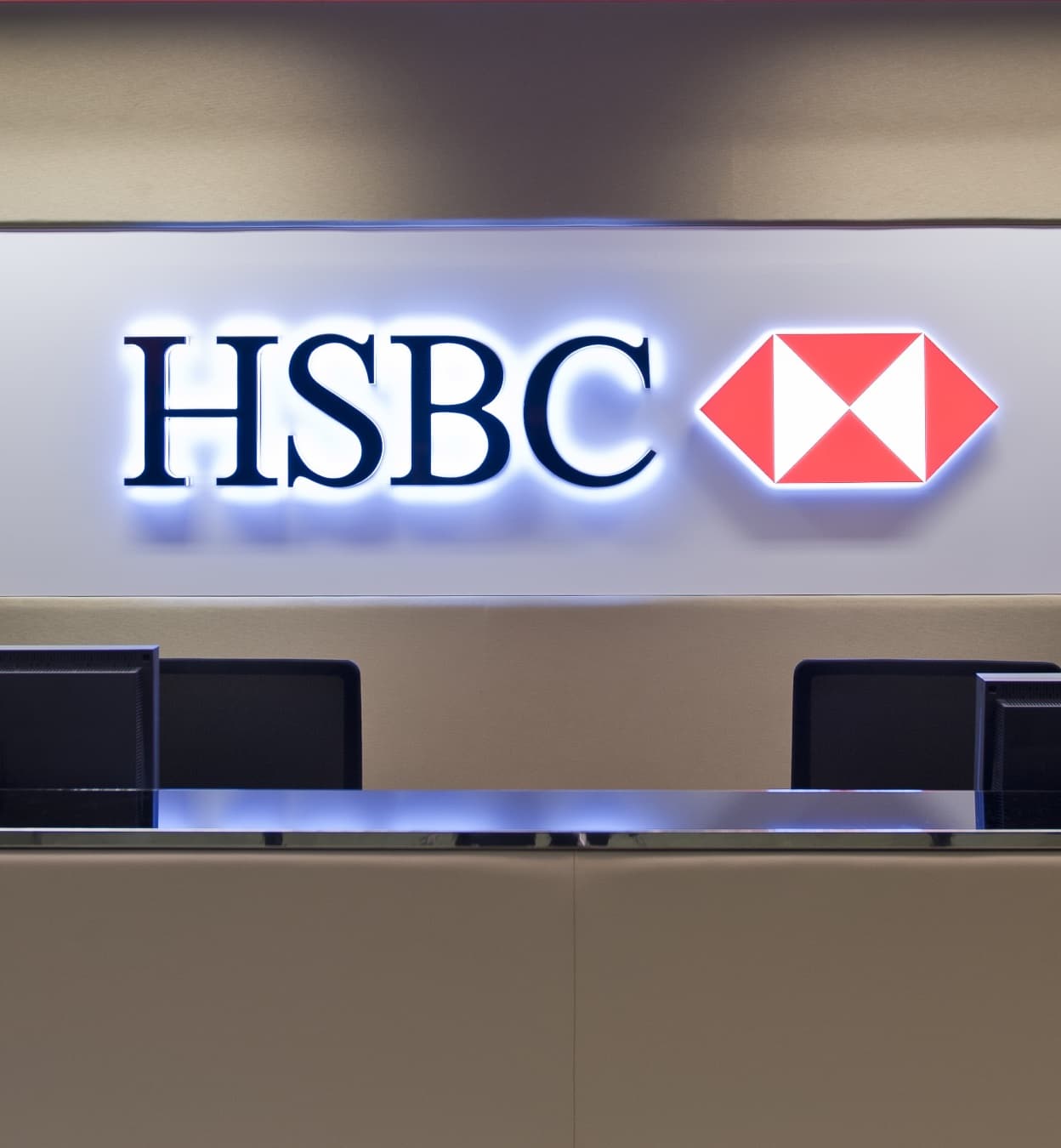 The HSBC lockup lit above a reception desk, twin monitors set into the counter below.