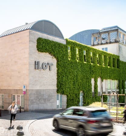 The ILOT building facade covered in ivy, the wordmark mounted on stone beside it.
