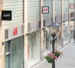 A row of ILOT storefronts including H&M along a pedestrian street.