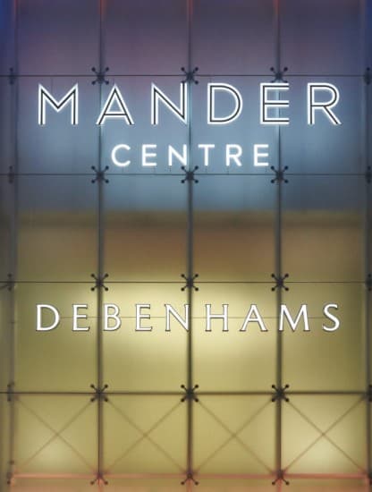 The Mander Centre and Debenhams lettering lit on the facade at dusk.