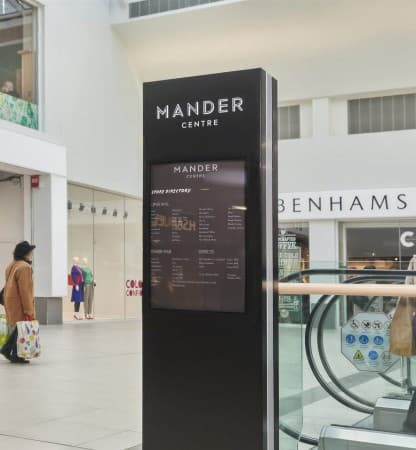A directory totem on the mall floor, storefronts running away behind it.