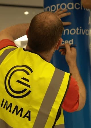 A GLIMMA installer applying vinyl lettering to a branded column.
