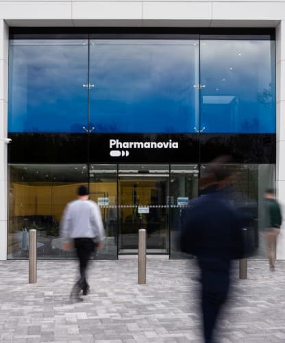 The Pharmanovia head office entrance at dusk, people walking past the glazed facade.