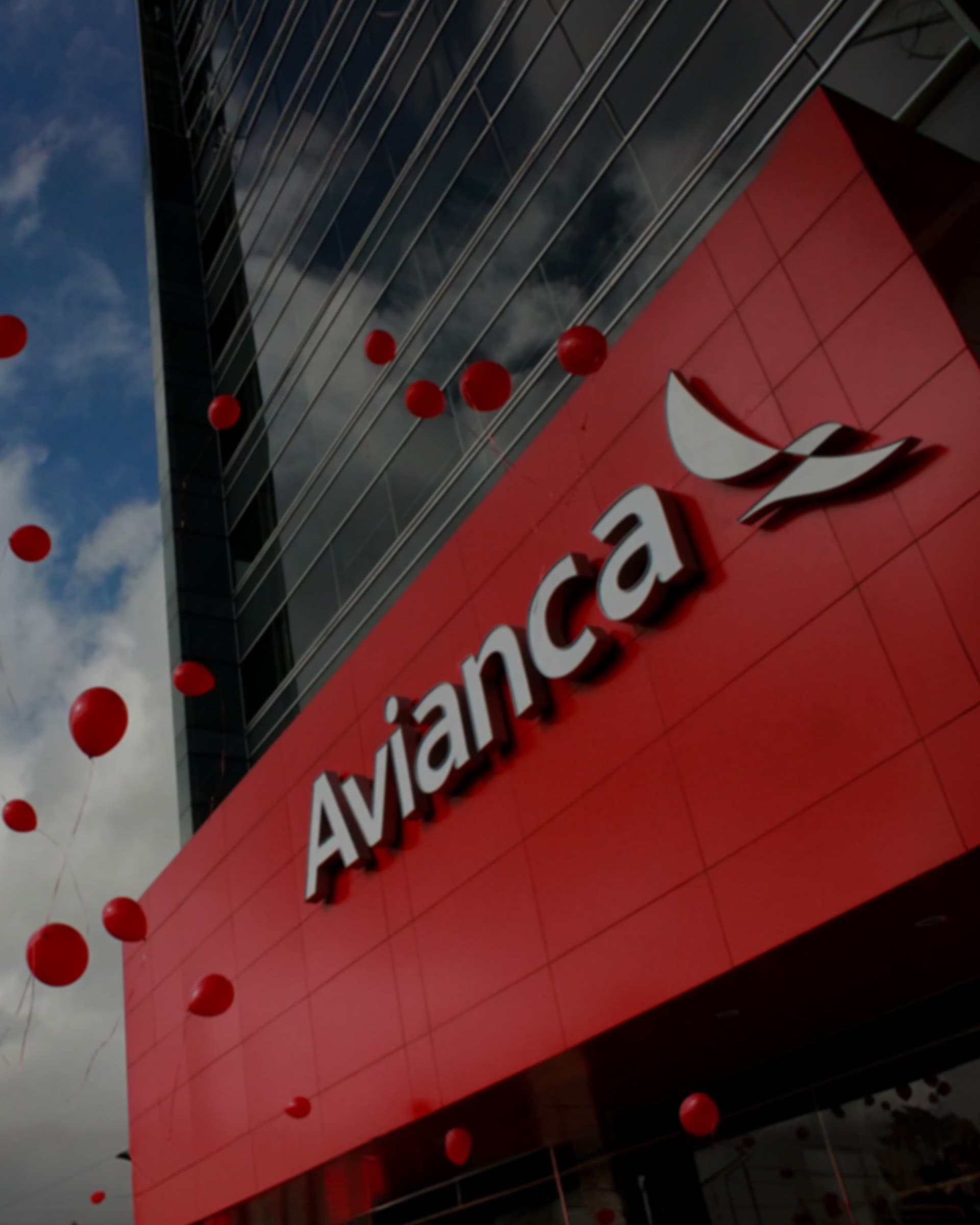 The Avianca headquarters seen from below, the wordmark and bird symbol on its red facade as red balloons rise past.