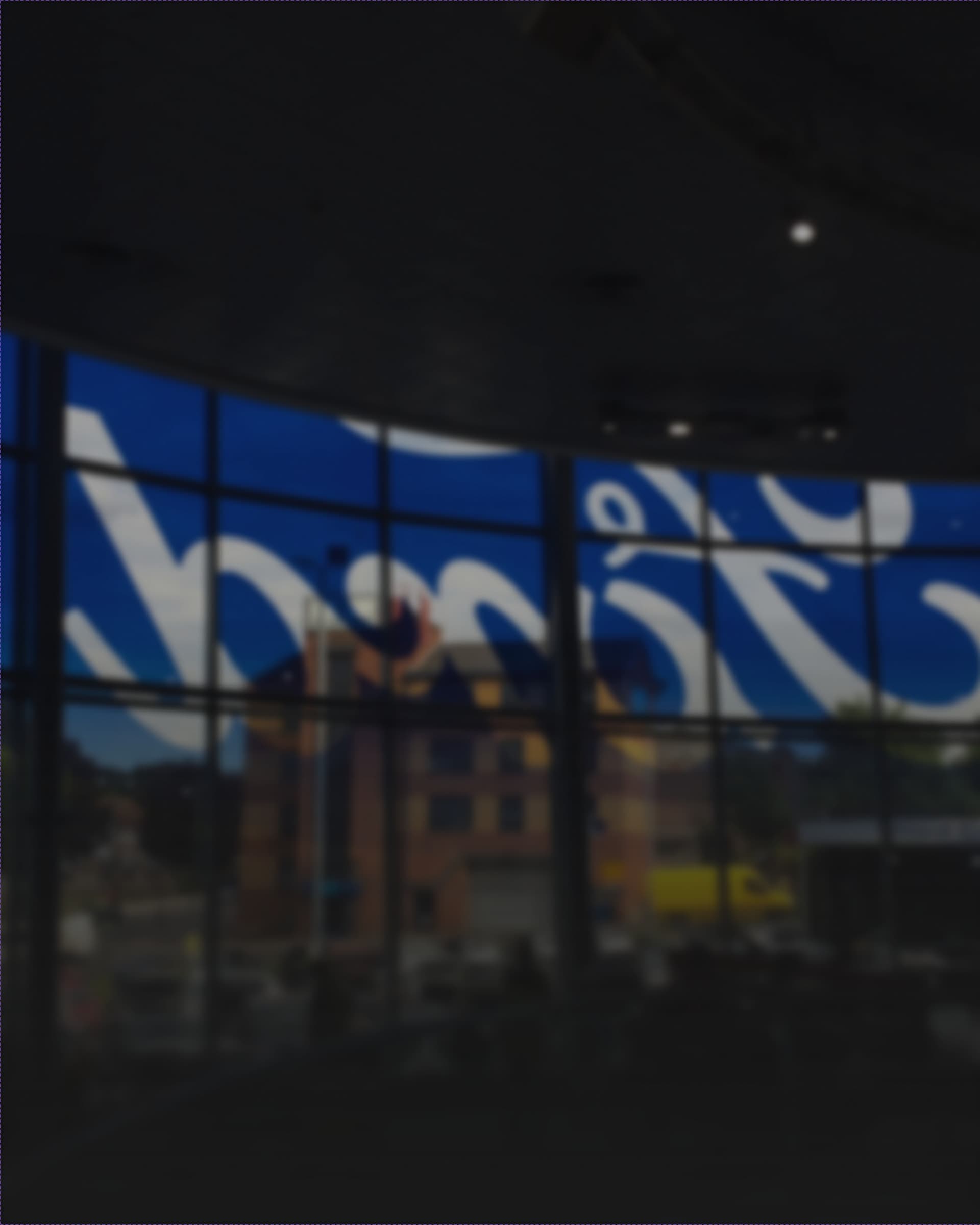 A Ford dealership at night, the illuminated Ford script running across its curved glass facade.