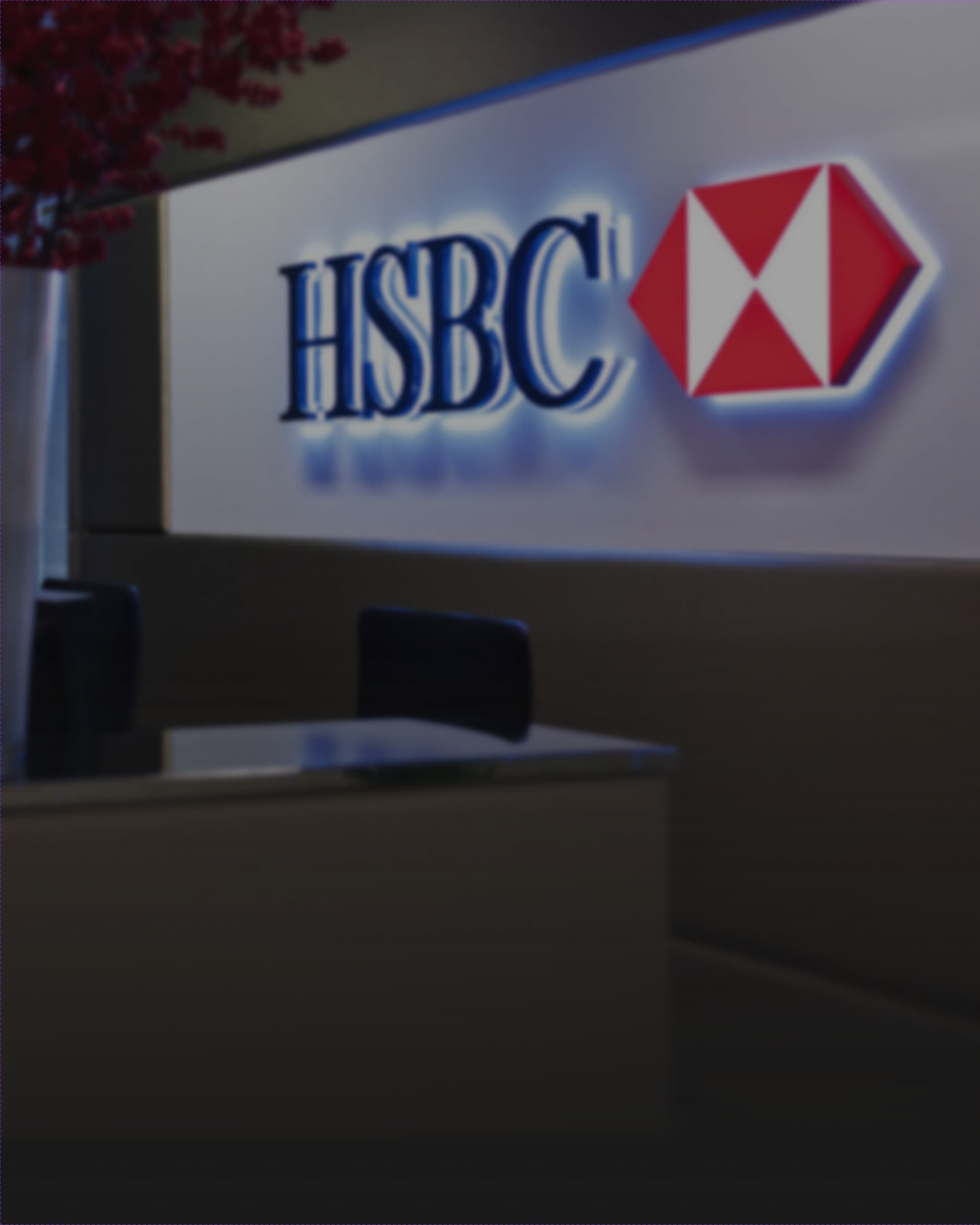 The backlit HSBC lockup and hexagon logo on a reception wall, red flowers in the foreground.