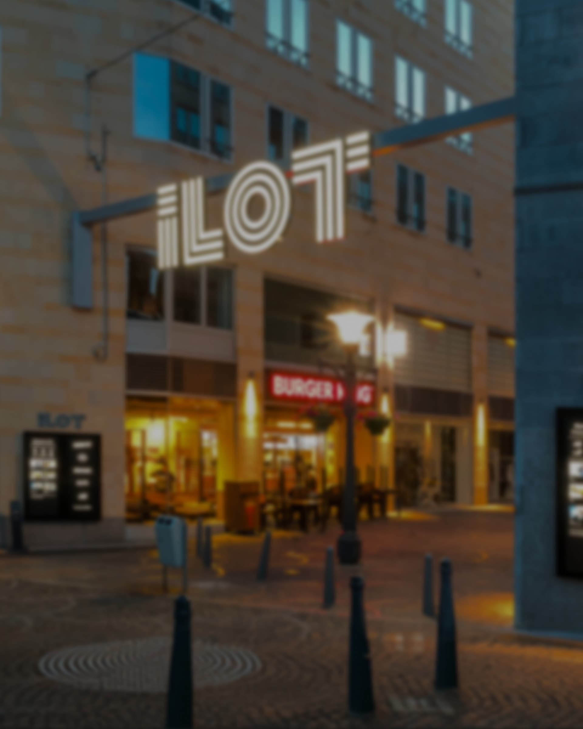 The illuminated ILOT gateway sign spanning a pedestrian street at dusk, shopfronts lit below.