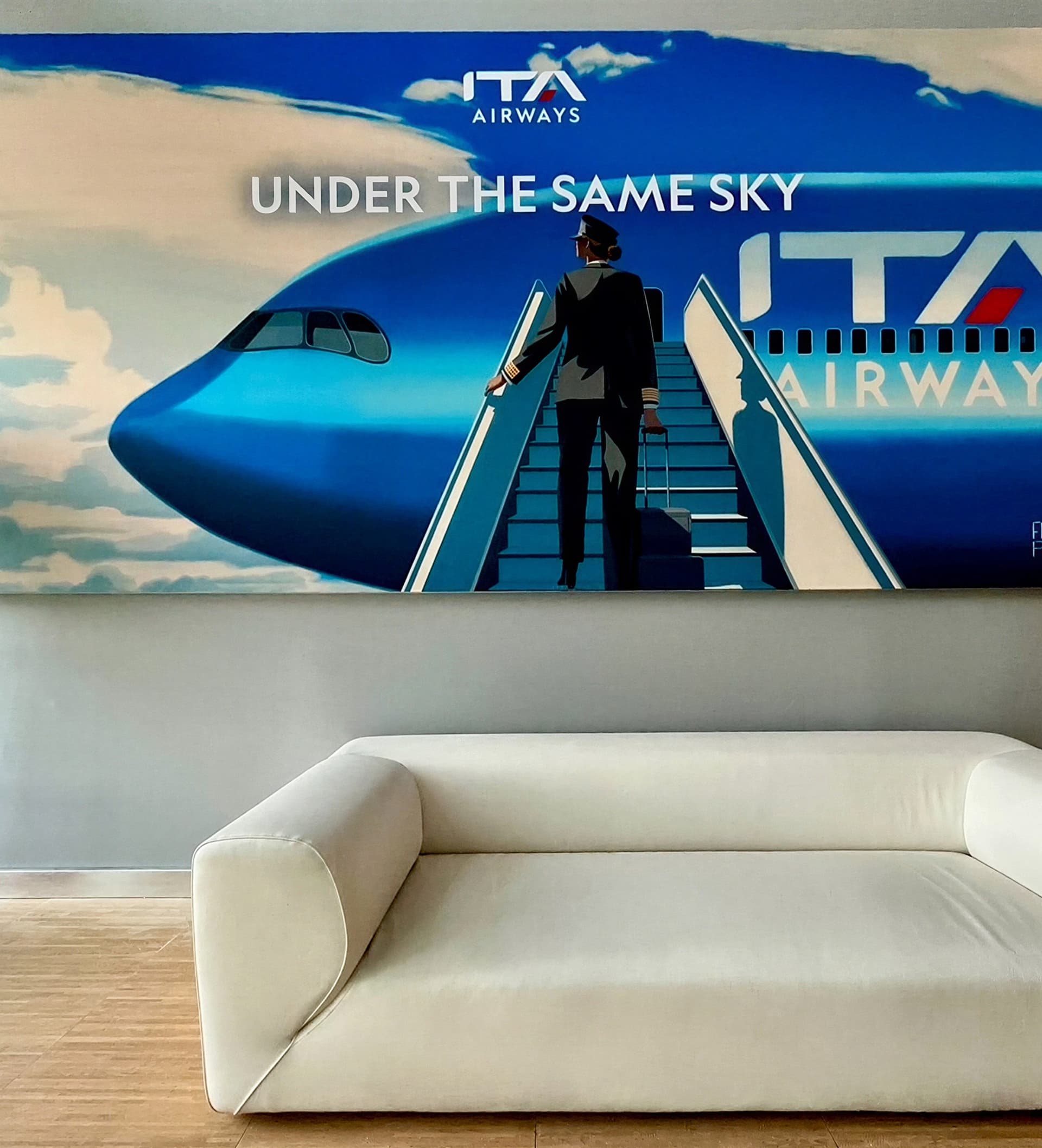 The “Under the Same Sky” mural above an ITA Airways lounge seating area.