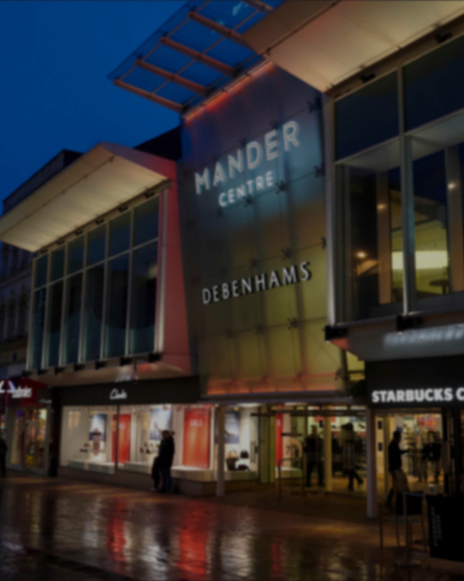 The Mander Centre entrance lit at dusk, the name above the doors.