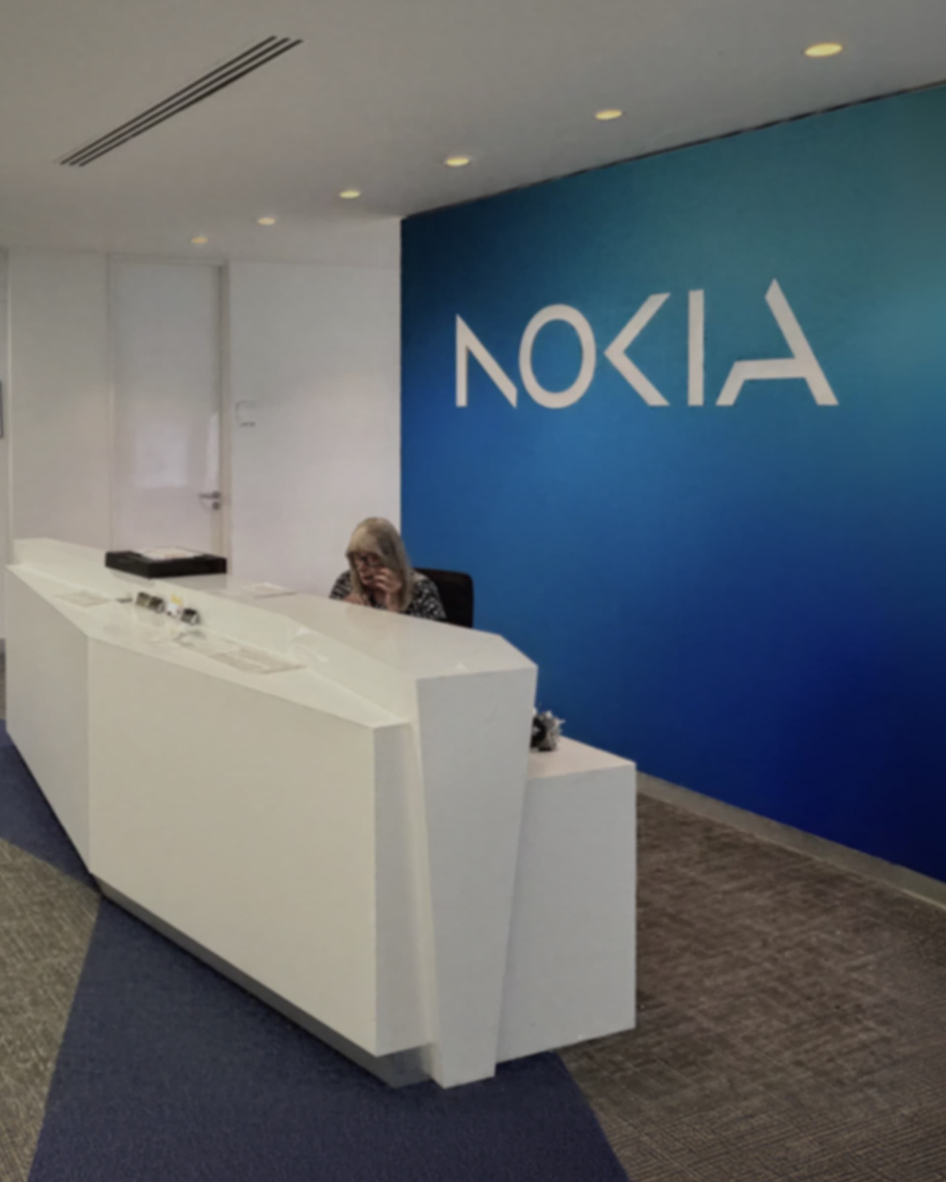 A receptionist seated at the white reception desk in front of the Nokia wordmark on a blue wall.