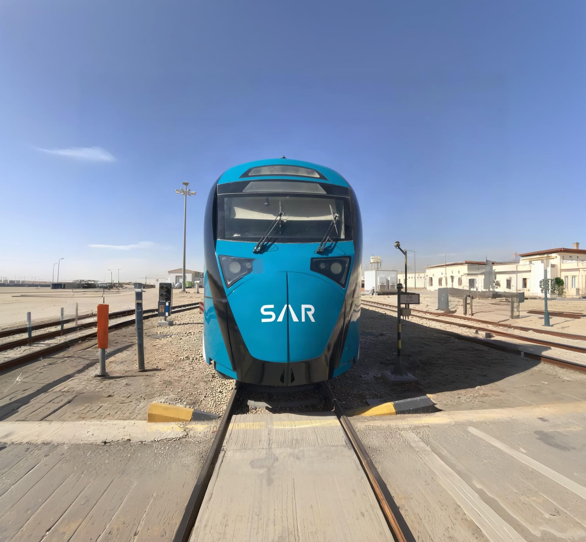 A SAR power car in its teal triple-layer livery, viewed head-on at a rail yard under open desert sky.
