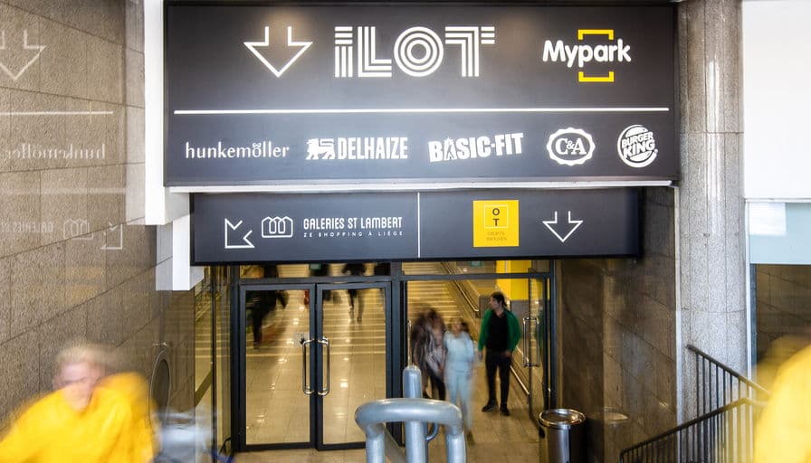An ILOT sign band over an entrance, arrows and retailer names above the doors.