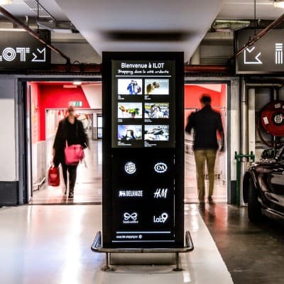 An ILOT directory totem in a shopping mall corridor, shoppers walking past on either side.