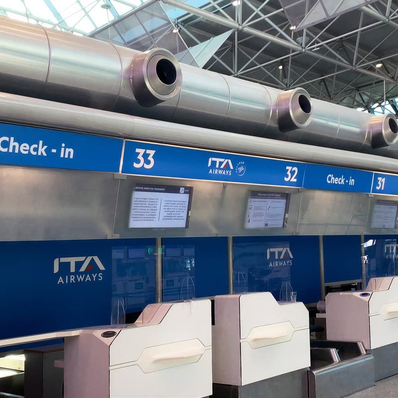 A row of rebranded ITA Airways check-in desks under the terminal roof.