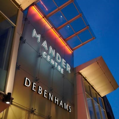 The Mander Centre and Debenhams lettering lit on the facade at dusk.