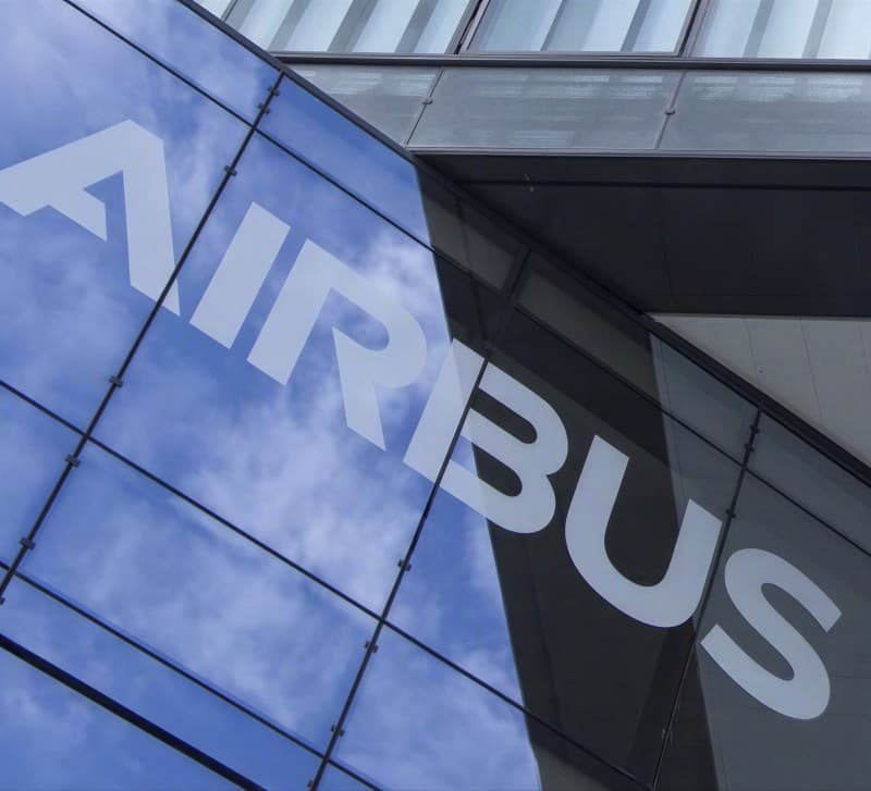 The Airbus wordmark on a glass building facade, reflecting a blue sky and clouds.