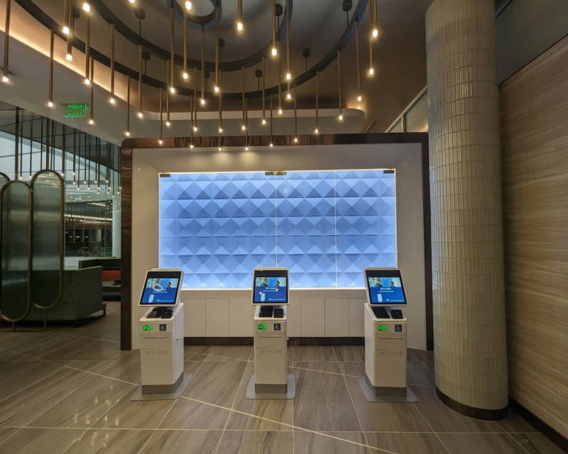 Self-service kiosks against the illuminated glass wall of a Delta Sky Club at Minneapolis–St Paul.