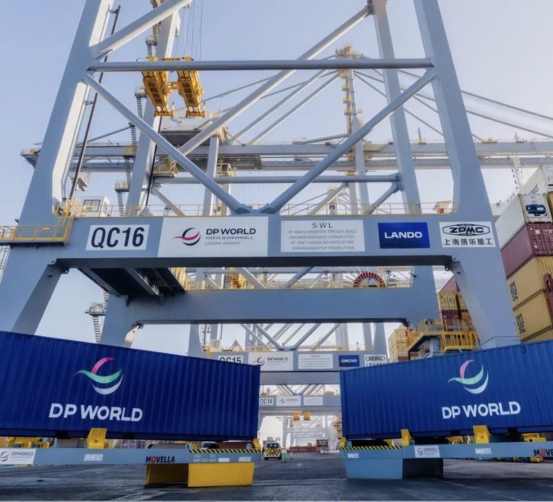 A DP World ship-to-shore crane at Santos, blue shipping containers lined up beneath its gantry.