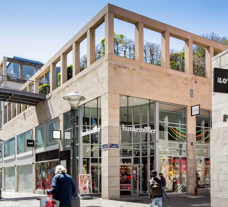 The ILOT corner building in daylight, glass shopfronts including Hunkemöller beneath the colonnade.