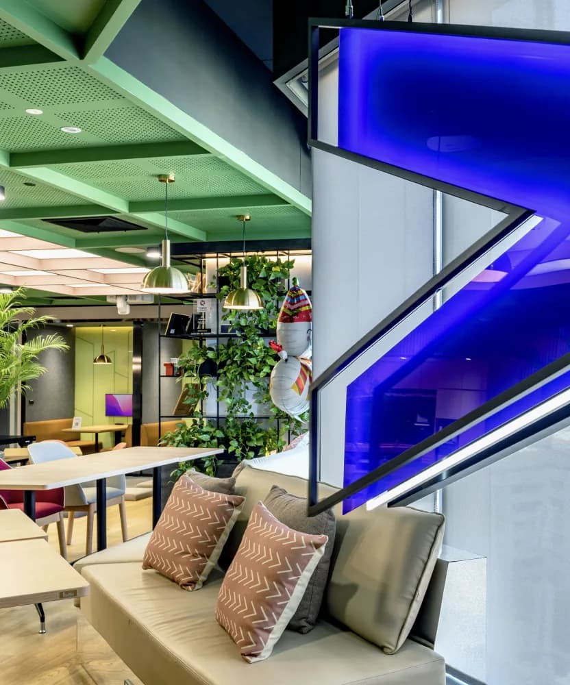 A break-out area with planting, pendant lighting and an illuminated blue brand sculpture