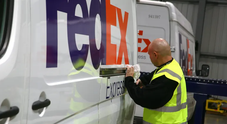 A FedEx technician applying vehicle livery to a branded van.
