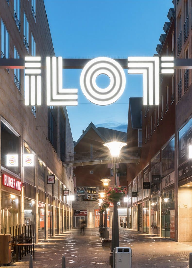 Illuminated iLOT signage over a retail and leisure street at dusk