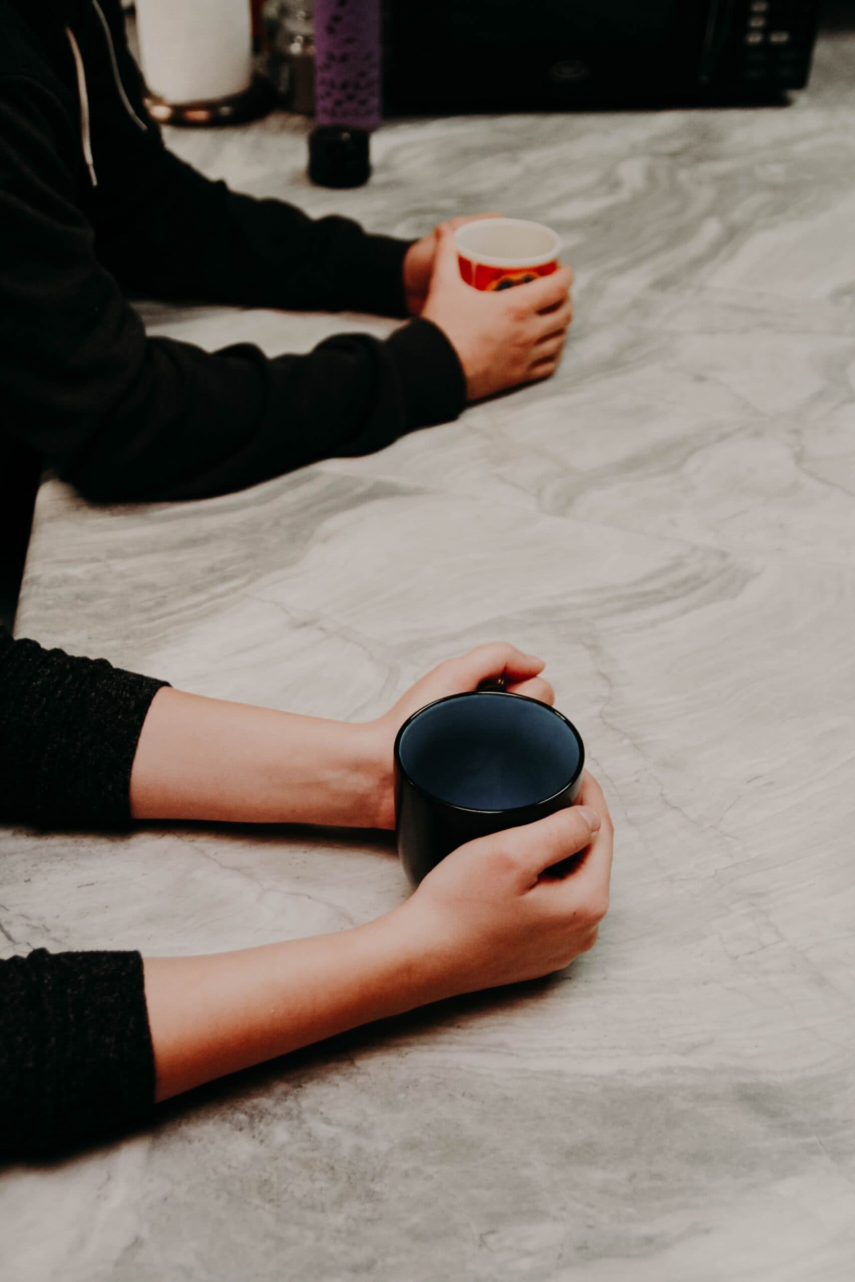 Two people sitting across a marble table, each holding a mug of coffee
