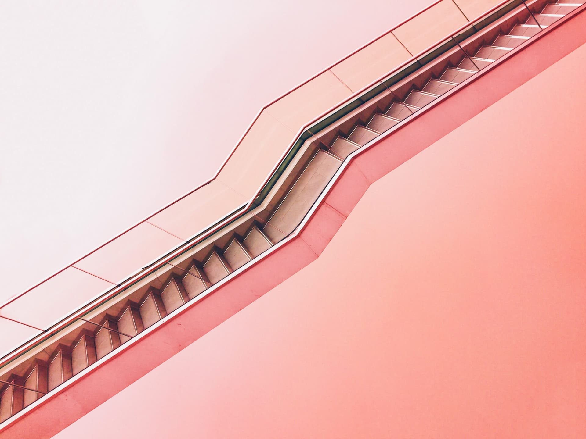 Underside of an escalator against a pink wall