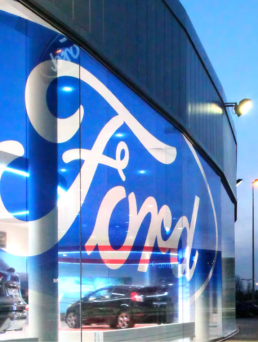 A Ford showroom interior looking out through curved glazing carrying the blue Ford wordmark